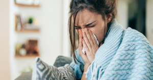A woman sneezing while wrapped in a blanket